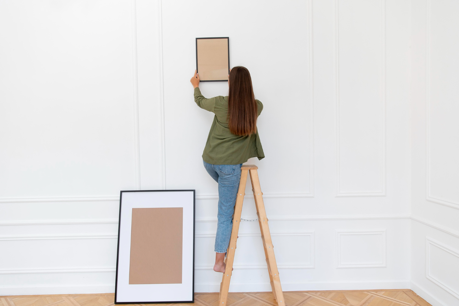 Mulher pendurando quadro na parede de casa Mulher pendurando quadro na parede de casa